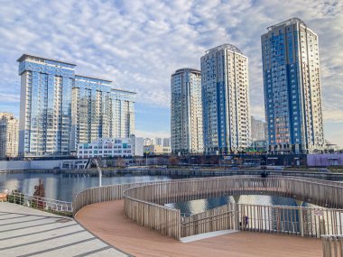 Modern yüksek binalar ve ahşap tahta kaldırımlı sakin bir rıhtım sahnesi manzaralı, rahatlama için dairesel oturma alanı sunan Kyiv, Ukrayna, 03-15-2024