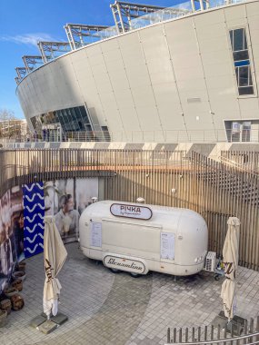 An outdoor scene with an INK trailer labeled HANSA, possibly for a mobile ad campaign, parked near a modern building with a glass facade and metal beams The setting sug Kyiv, Ukraine, 03-15-2024 clipart