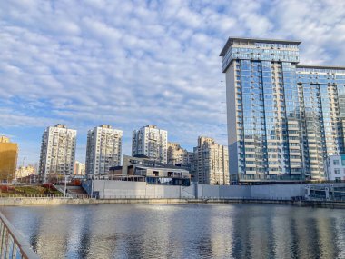 Sakin bir su, yürüyüş yolu, yeşillik, modern konut binaları, çağdaş mimari ve parçalı bulutlu gökyüzü Kyiv, Ukrayna, 03-15-2024