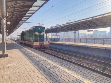 An old-fashioned train, possibly arriving or departing at a well-maintained station on a sunny day The image features brick paving, yellow safety markings, buildings, and e Kyiv, Ukraine, 03-15-2024 clipart