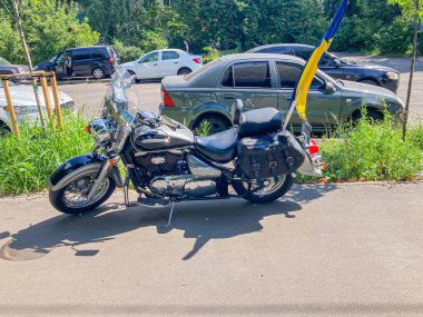 Yol kenarına ya da otoparka park edilmiş krom renkli ve eyerli siyah bir motosiklet. Arka planda Ukrayna bayrağı birçok Kyiv, Ukrayna, 06-15-2024 'te arabaları gösteriyor.