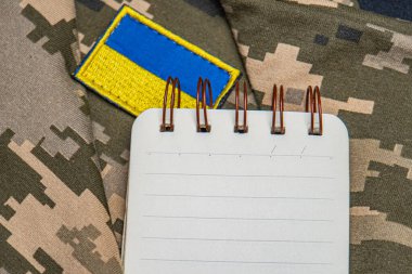 Askeri not defteri. Ukrayna bayrağı. Kamuflaj arka planında askeri temalı kişisel eşyalar serili. a