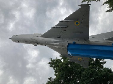 Image shows a gray, blue, and yellow single-seat fighter jet outside, likely at an exhibition or museum with weapon mounts Natural daylight lighting Kyiv, Ukraine 06-02-2024 clipart