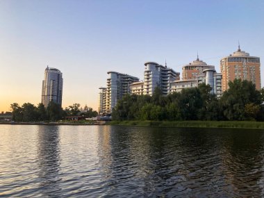 Alacakaranlıkta sakin bir şehir sahnesi, yansıtıcı bir su kütlesi, yemyeşil, modern yüksek binalar, ve uzaklara giden bir yol kompozisyon şekeri Kyiv, Ukrayna 06-02-2024