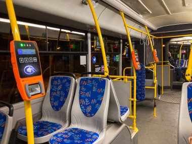 Interior of a bus, blue upholstered seats with white headrests, ticket validator or card reader near the seats, Fare Paid display, yellow safety rails between rows, orang Kyiv, Ukraine 06-02-2024 clipart