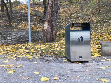 Muhtemelen ödeme ya da talimatlar için dijital ekranı olan modern metalik bir telefon kulübesi, sonbaharda bir parkta ya da bahçede yer almaktadır.