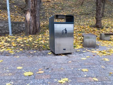 Görüntü, dağınık sarı sonbahar yaprakları arasında çöp tenekesi ya da ambalajlı bir açık hava sahnesini gösteriyor. Yol, beton kaldırım taşlarından yapılmış Kyiv, Ukrayna 06-02-2024