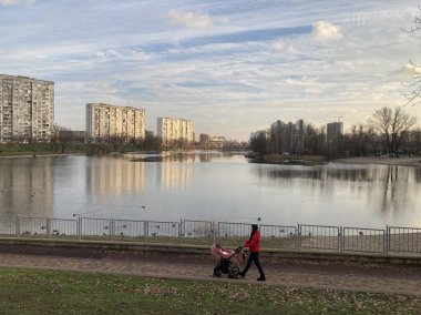 Sakin bir göl manzarası olan ve binaları yansıtan bir şehir parkı sahnesi, arka planda tek başına gezinen bir kişi Ukrayna, Kyiv, 11-02-2024 kentsel ikametgahını işaret ediyor.