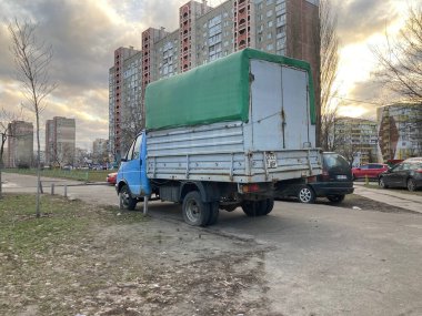 Yeşil ekipman kutusu olan eski, paslı mavi bir kamyon yol kenarında çimen olan bir şehir sokağında park halinde. Arka planda diğer araçlar görülüyor. Gökyüzü Kyiv, Ukrayna 11-02-2024