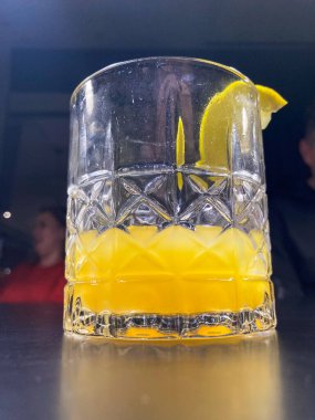 Görüntü kapalı bir odanın yakın çekimini gösteriyor, yapay olarak aydınlatılmış bir bardakta limon garnitürlü kokteyl. a