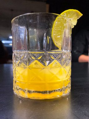 Masanın üzerinde cam bir kokteyl resmi, muhtemelen bir mimoza ya da sıcak ışıklandırmalı kapalı bir ortamda turunç rengi ve süslemeli Bloody Mary.