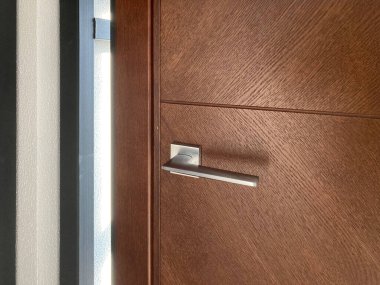 Dikey panelleri, gümüş gidon kolu ve yatay perdeleri olan minimalist ahşap bir kapının yakın plan görüntüsü.