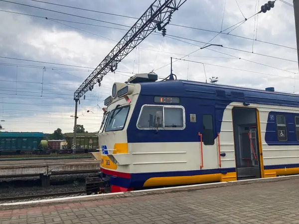 Gökyüzünün altındaki elektrikli bir demiryolu platformunda mavi, sarı önlü bir trenin gizli bir görüntüsü. Trenin pencereleri açık ve Kyiv, Ukrayna 06-02-2024