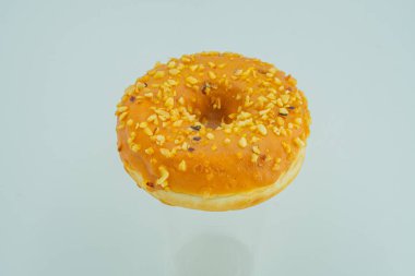 Görüntü, açık renkli yüzeyine sarı serpiştirilmiş turuncu bir donut serpiştirir, parlak bir iç aydınlatma altında sade bir arka planda.