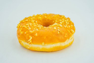 Tohum ya da fındık parçalı tek, taze görünümlü, sarı jöleli bir donut, tarafsız bir zemin üzerinde, açık bir yüzeyde oturur.
