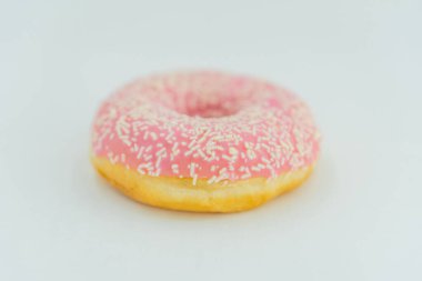 Pembe kremalı ve beyaz serpiştirilmiş tek bir altın-kahverengi donut düz bir arkaplanda gösteriliyor fotoğrafta yüksek kontrastlı aydınlatma var