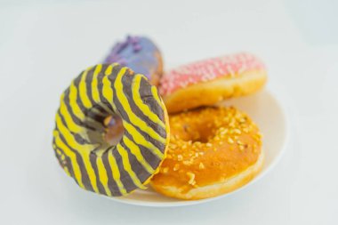 Image of a plate with three doughnuts, each decorated differently one striped yellow and purple, another plain, and the third dusted with orange sprinkles The plate has a reflective surface, and th clipart