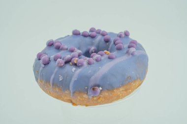 Görüntü, lavantalı, sanatsal olarak kıvrılmış veya serpiştirilmiş tek bir yuvarlak çörek gösteriyor. Küresel şekerleme topları zıt ve düz bir arkaplan üzerine kurulmuş. Tarz c 'yi gösteriyor.