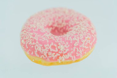 Beyaz serpiştirilmiş tek bir pembe kaplı donut, düz bir arkaplanda desenli bir yüzey ve açık bir iç mekan sergiliyor.