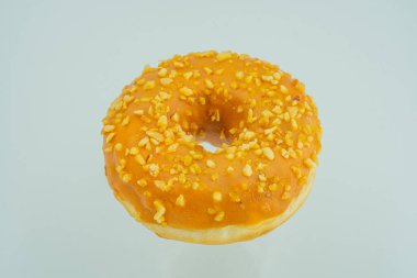 Tek, merkezi bir donut açık gri bir yüzeye dayanır, fındık serpiştirilmiş turuncu üzerine sade ışık serpiştirilmiş tatlı ikramların görünümünü vurgular