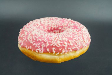 Tek, canlı, pembe jöleli donut desenli ve zıt şeker parçacıkları, altın kahverengi tabanlı, koyu bir arka planda ortalanmış.