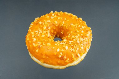 A centered, golden-brown doughnut on a light surface, with orangey-yellow icing and textured nutseed topping, photographed in a straightforward style for food context clipart