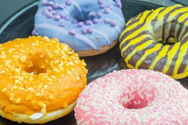 A tray holds six colorful doughnuts, each unique in design and topping The doughnuts include orange glazed, purple, and chocolate, decorated with sprinkles and nuts clipart