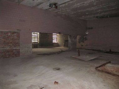 Kapalı, dağınık bir yer muhtemelen yenilenmiş ya da terk edilmiş tuğla duvarlar ve borular, döşemeler, müstehcen bir kapı çerçevesi, parmaklıklı pencere ve loş ışıklandırma.