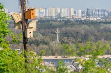 Wide panoramic view of an urban landscape with a river, green trees, elevated metal structure, boats, buildings residential, commercial, industrial, construction sites, overcast sky, no visible loc clipart