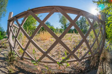 Image shows a wooden archway with an intricate lattice, possibly in a park or rural area The background suggests a garden or courtyard with plants and trees Naturalistic style, late afternoonearly clipart