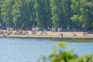 Renkli şemsiyeler, alçak binalar, sakin sular ve yemyeşil bitki örtüsüyle dolu canlı bir sahil manzarası, mimarinin Kyiv, Ukrayna 06-17-2024 ile uyumlu olduğu huzurlu bir kıyı toplumunu akla getiriyor.