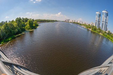 Mavi gökyüzü ve uzak kentsel binaların yansımalarıyla çağdaş bir köprüden sakin bir görüntü mimariyle Kyiv, Ukrayna 06-17-2024 'ün uyumlu bir karışımını sergiliyor.