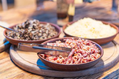 İçinde kavrulmuş fındık tohumu, kıtır pastırma ve rendelenmiş peynir bulunan ahşap bir tepsi resmi. Büyük ihtimalle yemek hazırlıkları sırasında, kapalı bir ortamda alınmış parmesan peyniri.