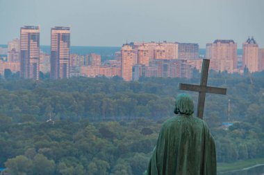 Görüntü, tepenin üstünde haç tutan, şehir manzarasına bakan bir kişinin heykelini gösteriyor. Hiçbir silah veya askeri teçhizat görünmüyor Kyiv, Ukrayna 08-24-2024
