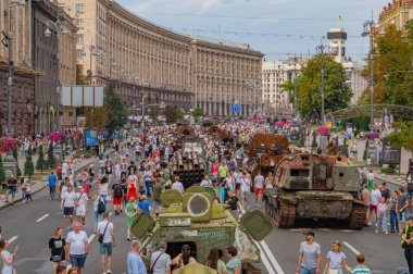 Görüntü, büyük olasılıkla Rusya-Kyiv, Ukrayna 08-24-2024 bağlamında siyasi veya askeri mesajlar taşıyan kalabalığın arasında sergilenen modern bir ana savaş tankının yer aldığı bir şehir sokak sahnesini gösteriyor.