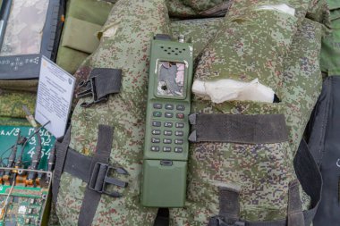 Görüntü, üzerinde modifiye edilmiş bir iletişim cihazı bulunan bir kamuflaj sırt çantası gösteriyor. Telsiz ya da cep telefonu ve anten olabilir. Olay yeri askeri kullanım olduğunu gösteriyor, muhtemelen Kyiv, Ukrayna 08-24-2024