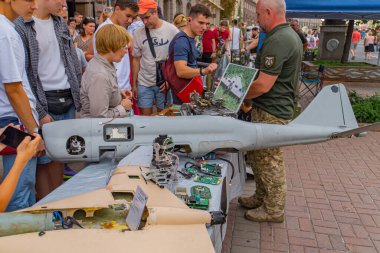 Ziyaretçi ve silah uzmanı olan bir savaş uçağının açık gövdesinin yer aldığı askeri uçak parçalarının sergilendiği sergi, açık havada, Possi Kyiv, Ukrayna 08-24-2024