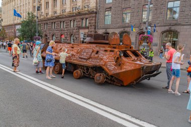 Eski bir askeri araç, muhtemelen bir tank ya da zırhlı araç, halka açık bir caddeye park edilmiştir. Koşulları çatışmanın kullanıldığını gösteriyor ve çeşitli işaretler Ukrayna 08-24-2024 'e ait olduğunu gösteriyor.