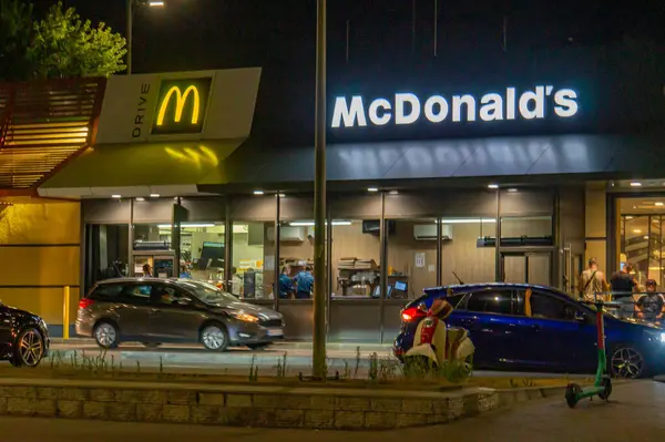 Görüntü, geceleri McDonalds 'ın fast food restoranını gösteriyor. Otoparkı ve Kyiv, Ukrayna 08-24-2024 numaralı aracın yanında bir kişi var.
