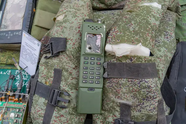Görüntü, üzerinde modifiye edilmiş bir iletişim cihazı bulunan bir kamuflaj sırt çantası gösteriyor. Telsiz ya da cep telefonu ve anten olabilir. Olay yeri askeri kullanım olduğunu gösteriyor, muhtemelen Kyiv, Ukrayna 08-24-2024