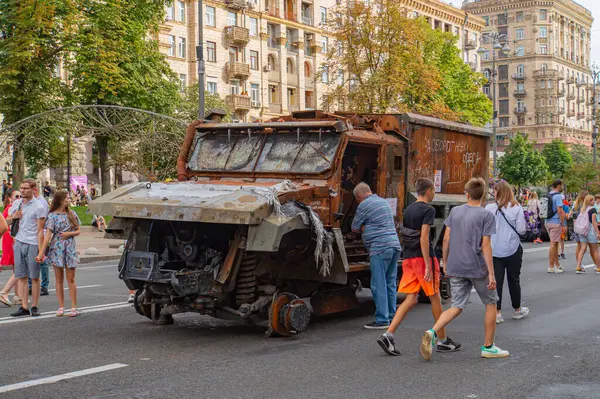 Görüntü ağır hasarlı bir askeri araç gösteriyor, muhtemelen zırhlı bir personel taşıyıcı ya da benzeri, uzun süreli savaş kullanımına işaret ediyor. Konum kentsel, muhtemelen Kyiv, Ukrayna 08-24-2024