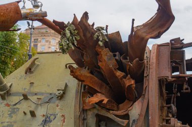 Eski, paslı bir askeri tank, tarihi ya da askeri bir yerin ortasındaki bir açık havada resmedilmiş. Araç bozulma ve aşınma belirtileri gösteriyor. Bulutlu gökyüzü kasvetli atmosp 'a ekleniyor.