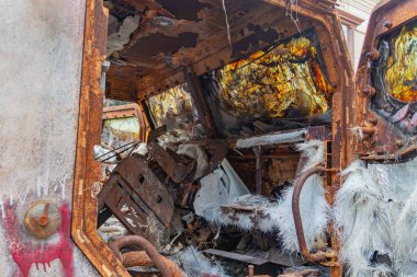 Çirkin, sanatsal bir fotoğraf hasarlı, paslı bir aracı gösteriyor. Görünür bir iç iskeleti var. Kırmızı grafiti yapılmış, tozlu zeminde duruyor.