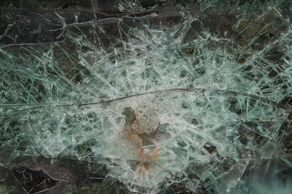 Cam yüzeydeki kurşun deliğinin yakın görüntüsü örümcek ağı benzeri çatlaklar, yuvarlak karanlık nokta, parçalanmış cam parçaları, ek bir bağlam yok.