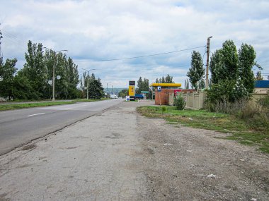 Görüntü, eski asfalt yolu ve yamalı toprak omuzlu kırsal ya da yarı kırsal bir yol gösteriyor. Sarı bir bina, muhtemelen bir mağaza ya da benzin istasyonu, Ri Kostiantynivka, Ukrayna, 06-15-2013