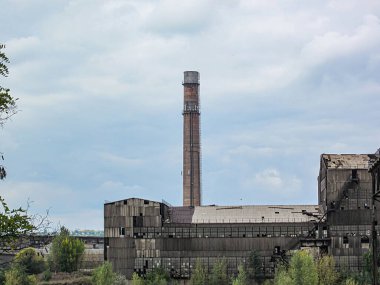 Büyük, tuğla bir endüstriyel yapının muhtemelen bir fabrika veya uzun bacası ve birden fazla havalandırması olan bir üretim tesisi. Kompleksin sıralı pencereleri var, Kostiantynivka, Ukrayna, 06-15-2013