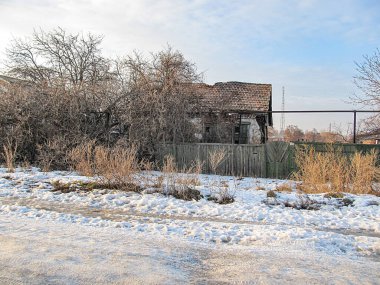 Yıpranmış bir evi ve ahşap çitli bir gökyüzü olan karla kaplı bir cadde, muhtemelen kış öğleden sonra Kostiantynivka, Ukrayna, 01-15-2013