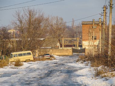 Görüntü, kar yağışlı bir kış sokak sahnesi, kenarda park edilmiş eski bir minibüs, çıplak ağaçlar, bir bina, elektrik direkleri ve bulutlu gökyüzü Kostiantynivka, Ukrayna, 01-15-2013
