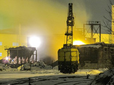 Bir sanayi bölgesinde kış gecesi sahnesi. Karlı zemin çevre ışığını yansıtıyor, uzun metal vinç, far yüklü sarı kaplar, koyu renkli Kostiantynivka, Ukrayna, 01-15-2013