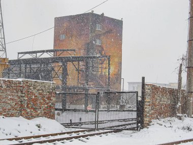 Büyük bir duvar resmi sergilenen eski, yıpranmış bir sanayi binasıyla karlı bir sahne. Duvar, at figürleri No v Kostiantynivka, Ukrayna, 01-15-2013